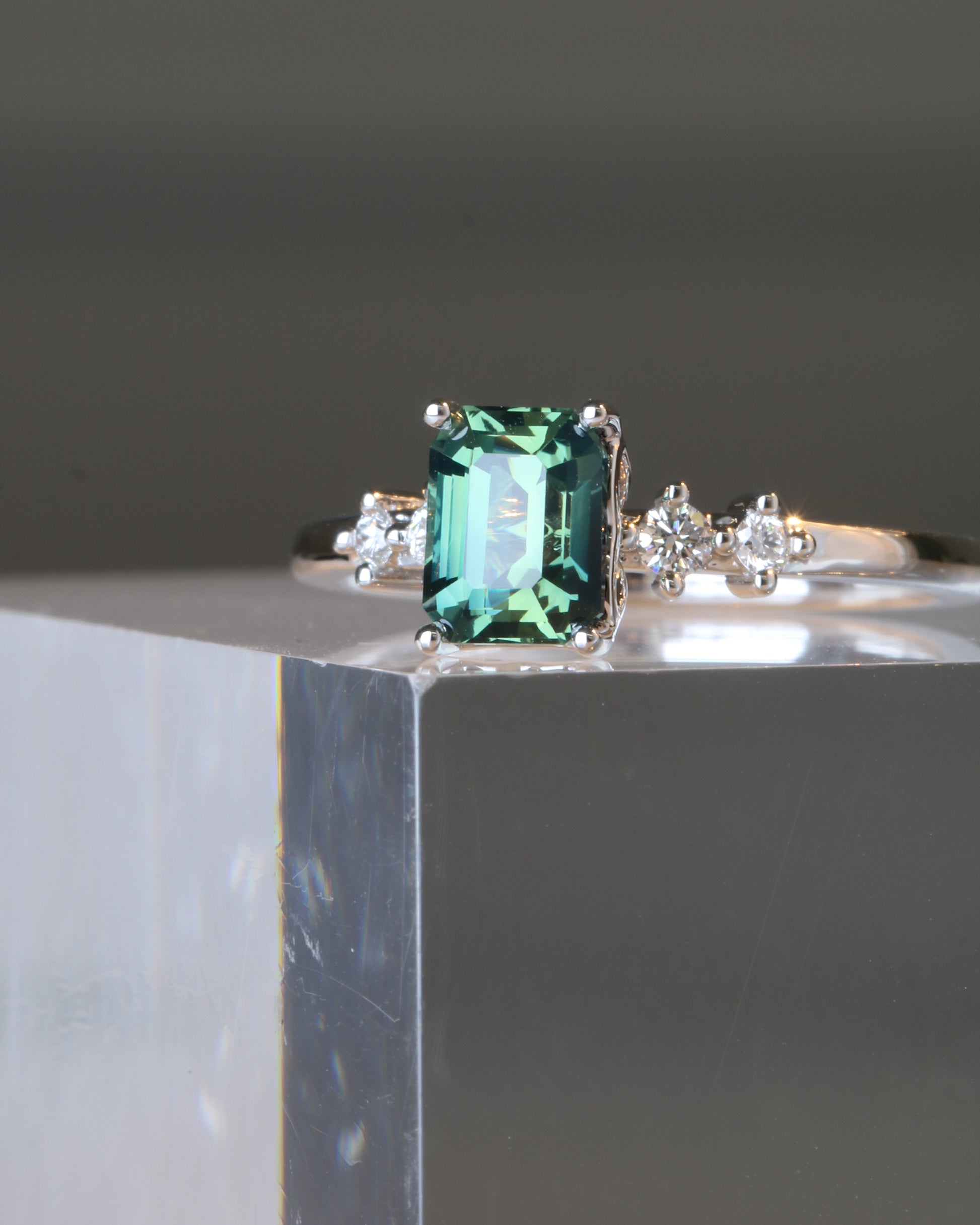 18k white gold teal Green sapphire ring on a glassy cube surface