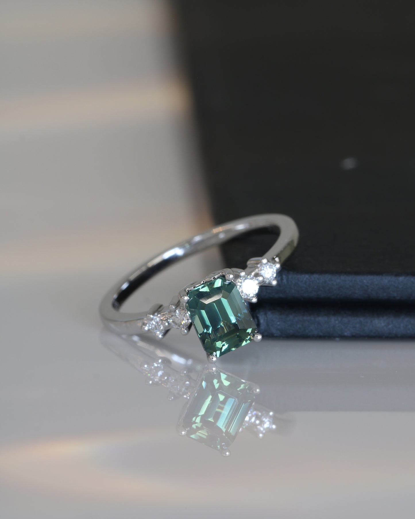 18k white gold teal Green sapphire ring on a reflective surface.