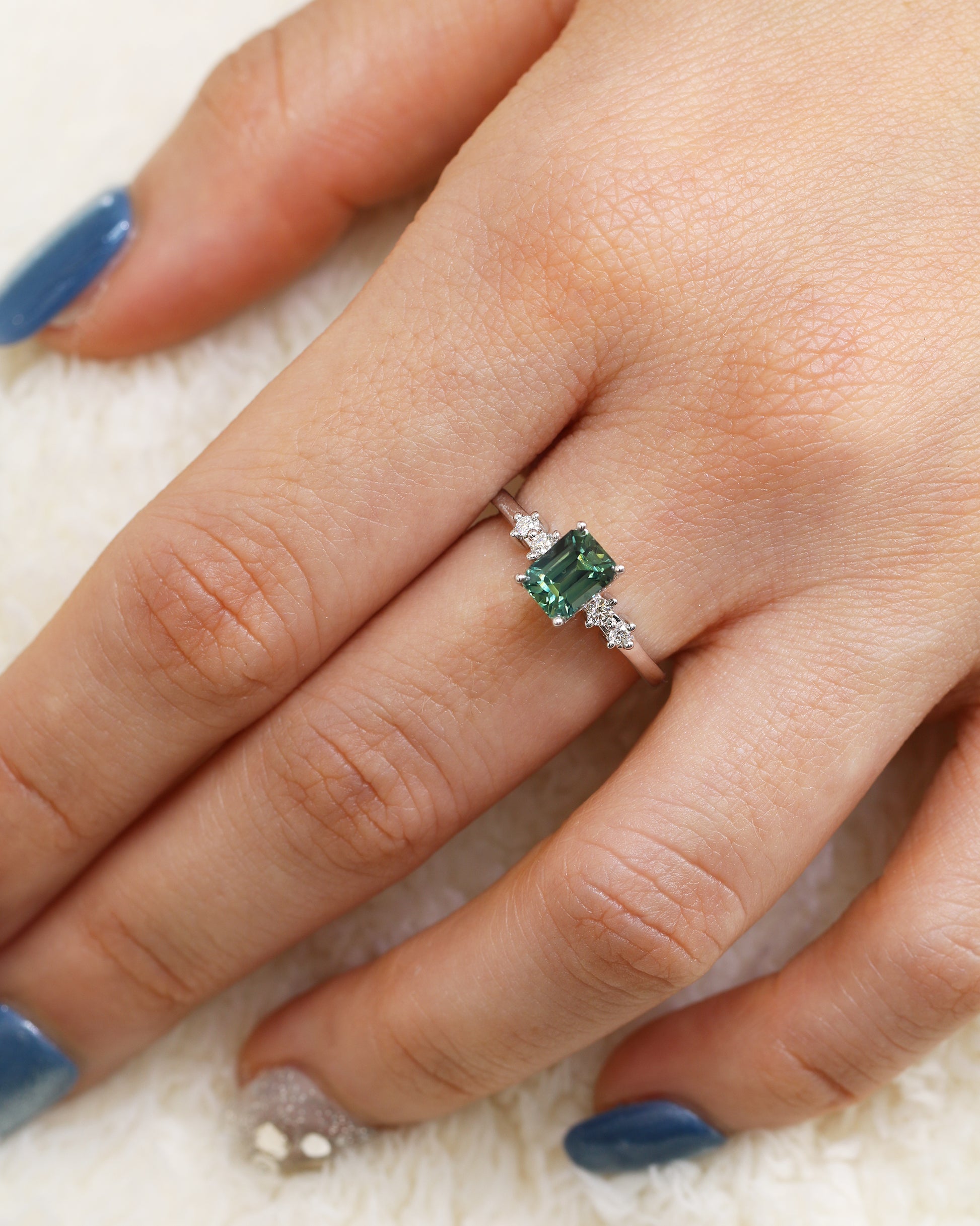 Hand wearing a 18k white gold teal Green sapphire ring  on a soft surface