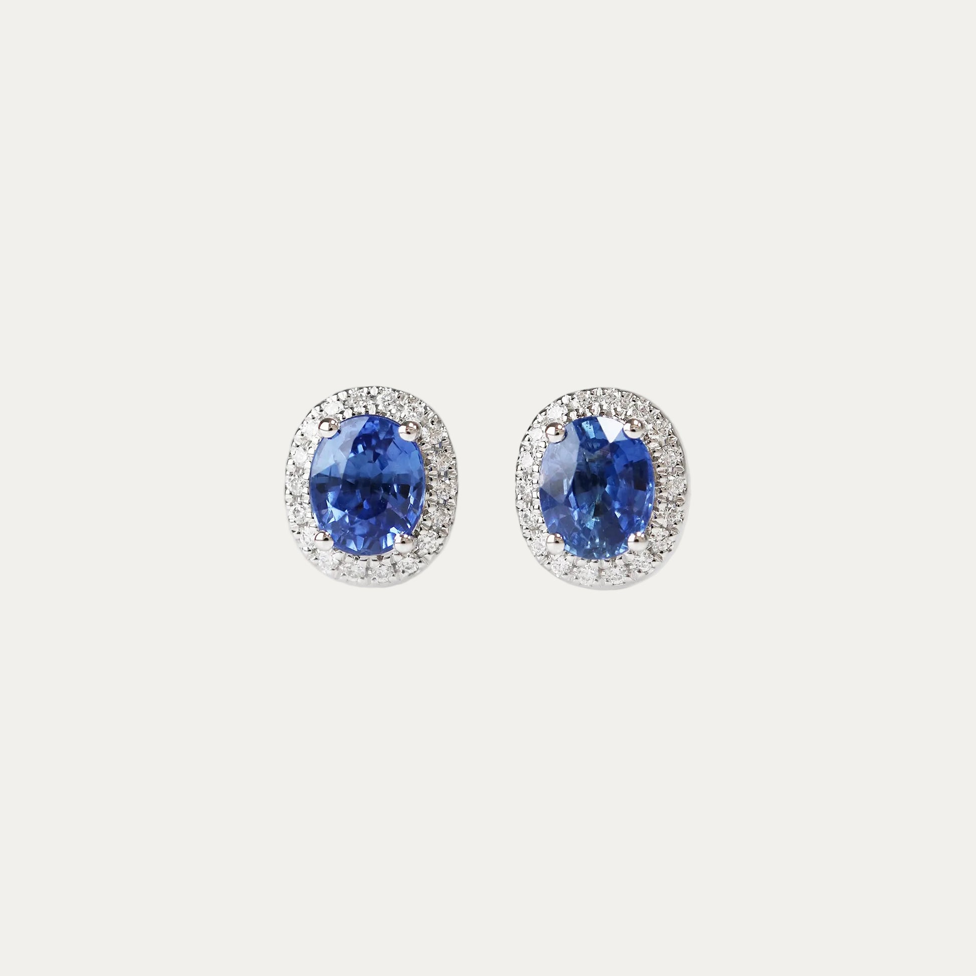 Pair of oval shaped cornflower sapphire earrings on a light gray background