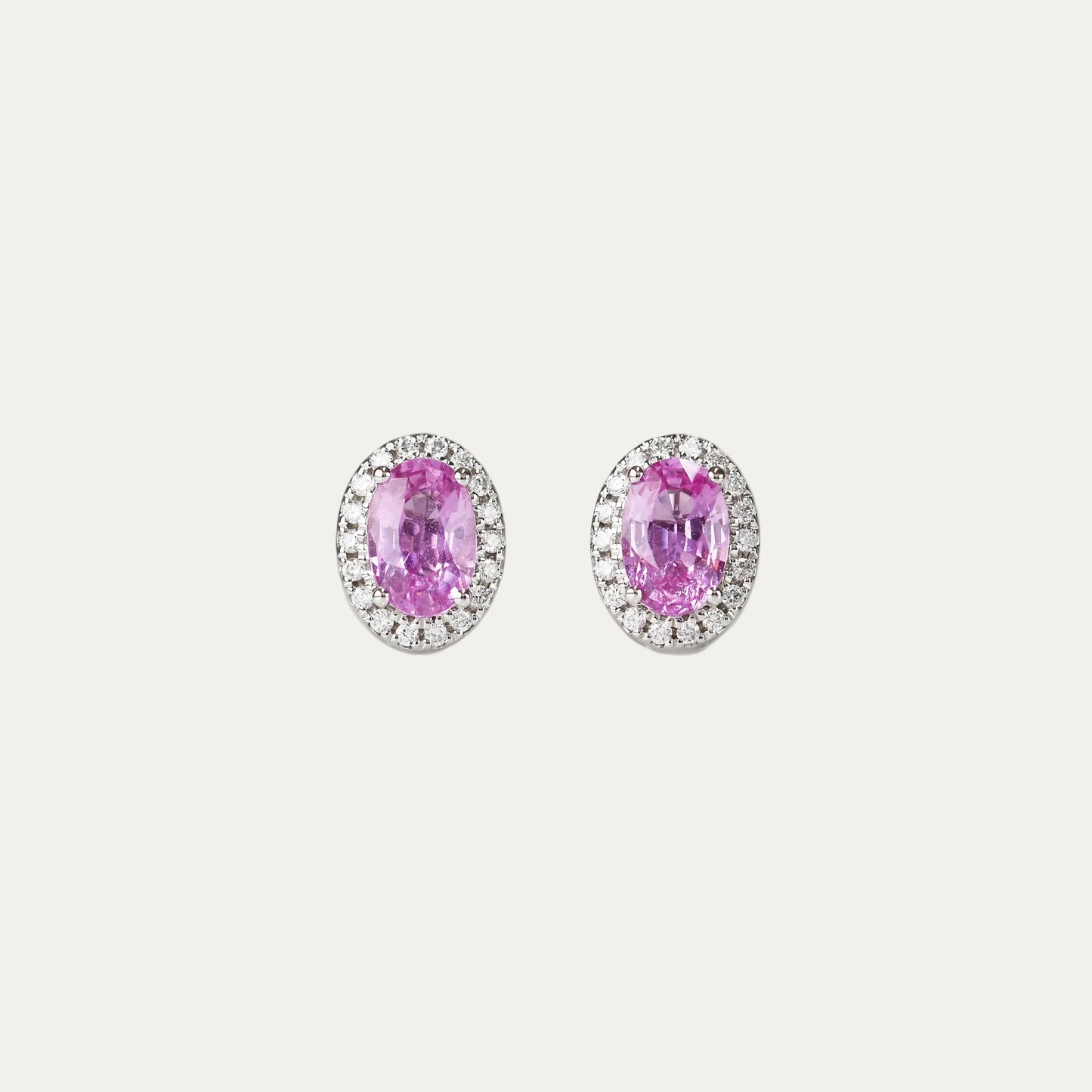 Pair of oval-shaped pink sapphire halo diamond earrings on a gray background